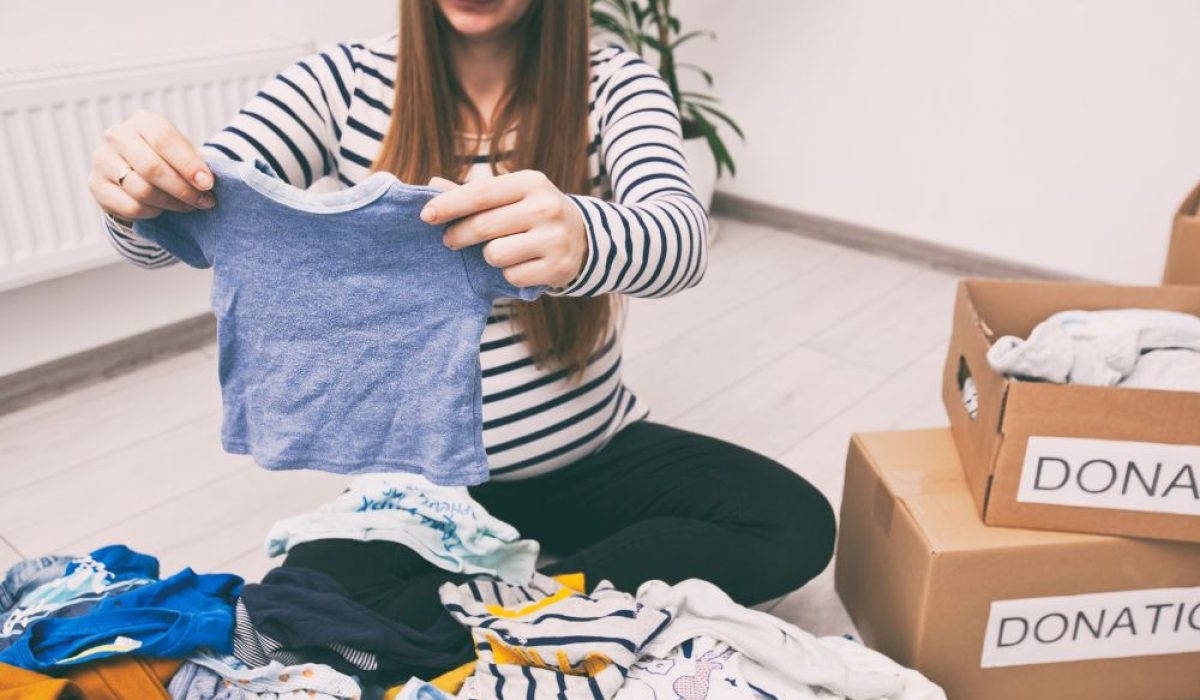 Parent decluttering baby gear and organizing toys into storage bins for a toddler room upgrade.