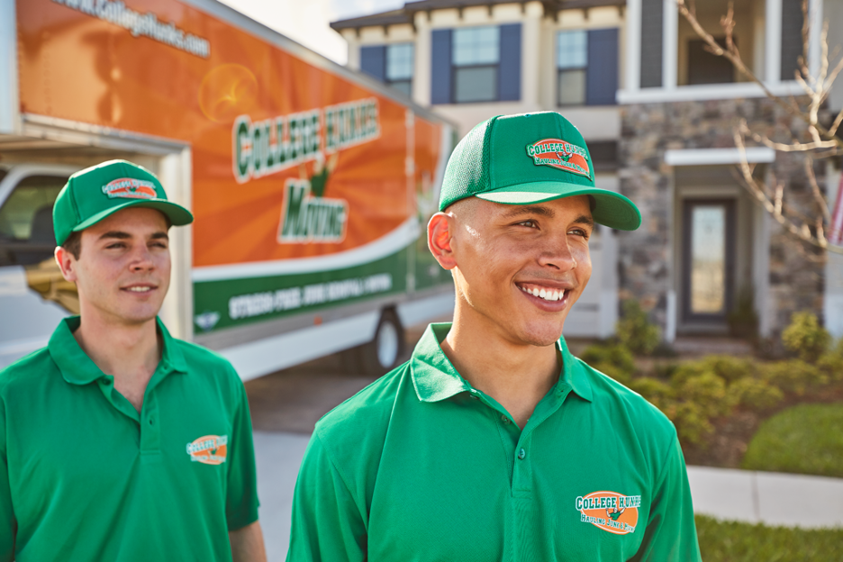 Two College HUNKS movers standing in front of a moving truck and a home, smiling.