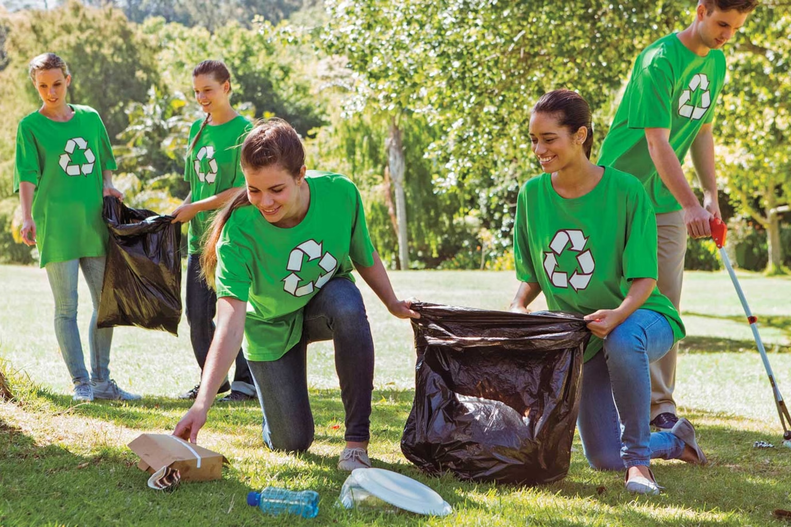 Volunteers in green recycle shirts collecting litter during a park cleanup