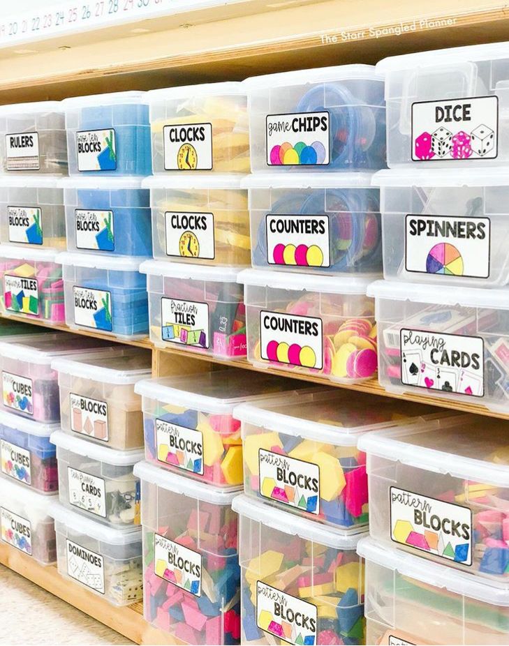 Labeled plastic bins with organized classroom supplies on shelves.