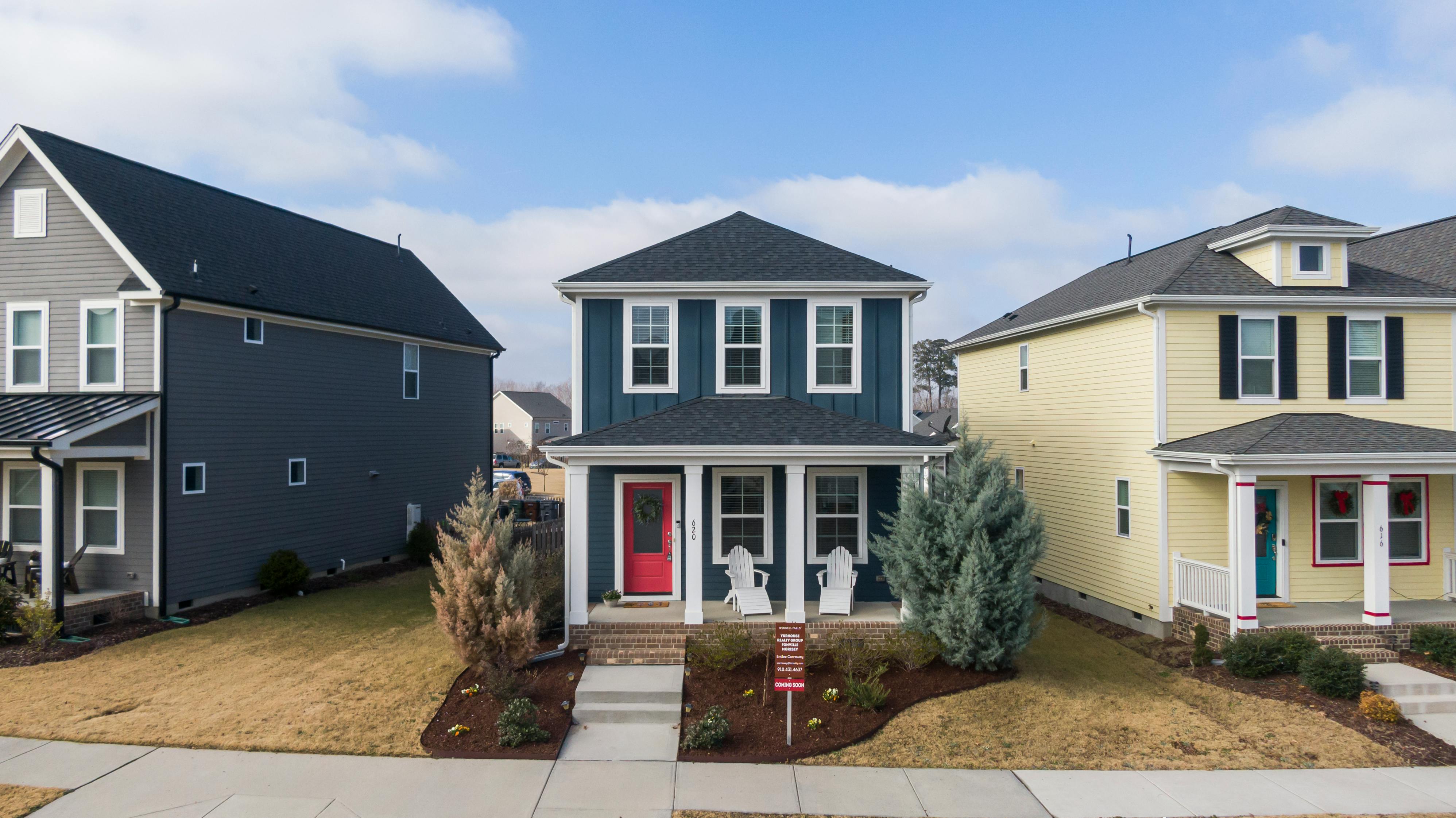 A two-story suburban blue home with a red door and a landscaped front yard