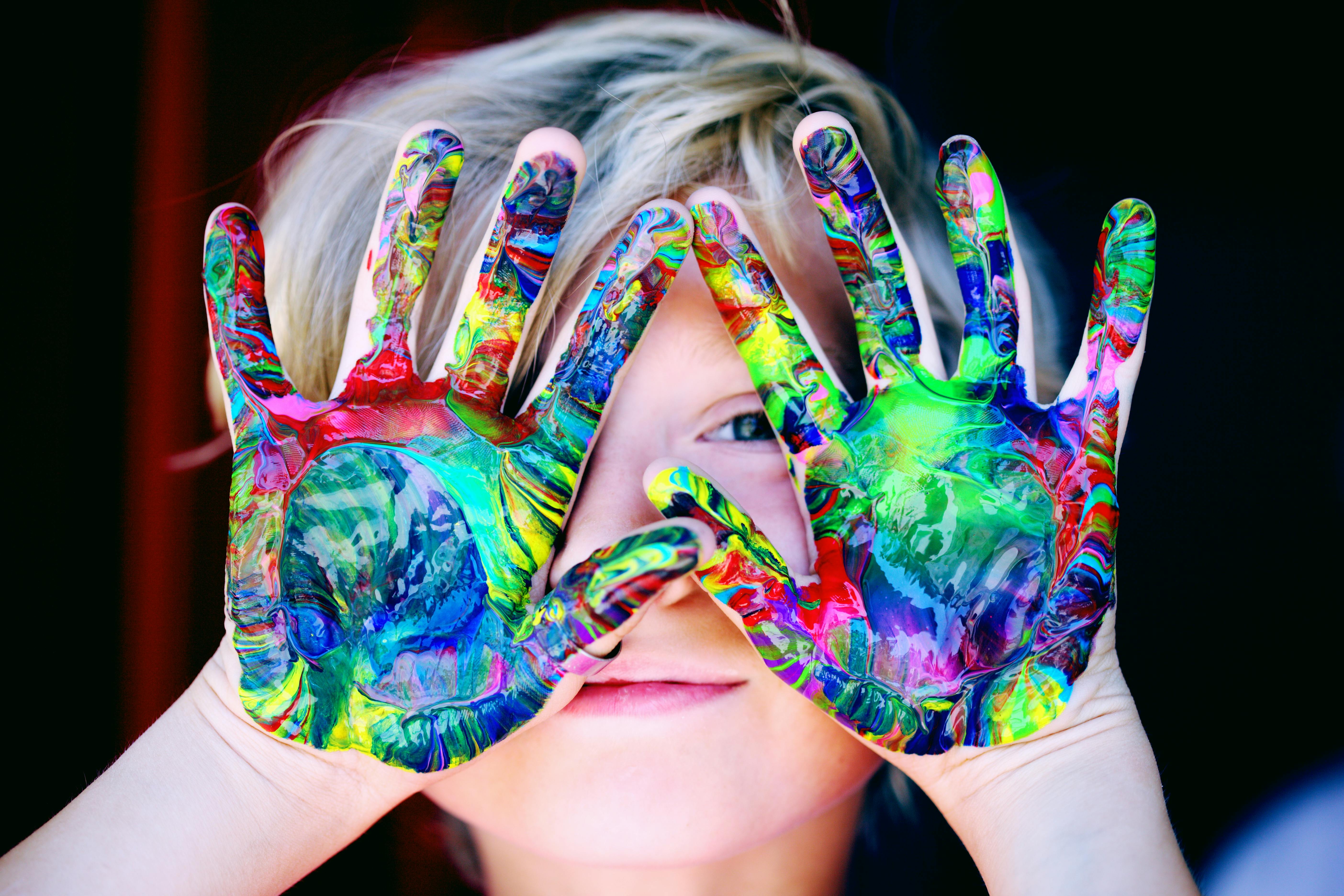 A young kid holding their painted palms up to their face, facing outwards