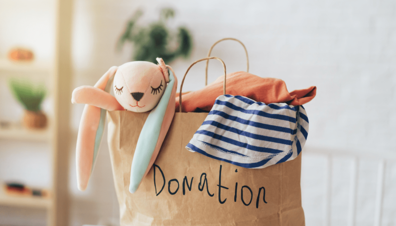 Paper bag labeled donation filled with children’s clothes and a stuffed bunny toy