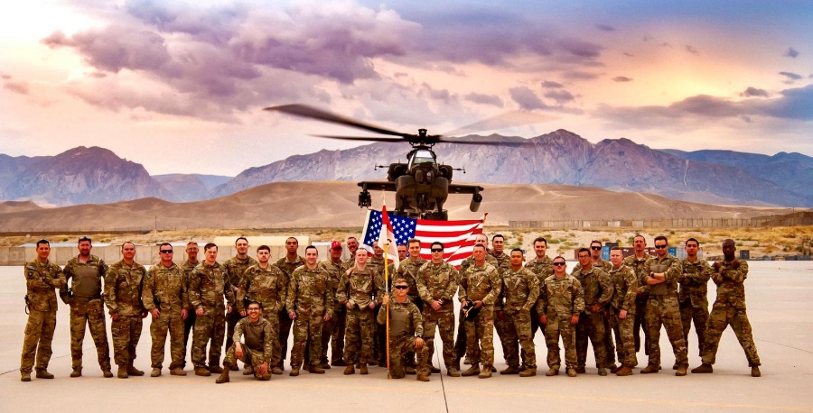 US Military and College HUNKS franchise owner hold US Flag in front of an Apache helicopter.