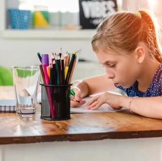 Young girl focused on doing homework at a desk with pencils and school supplies.