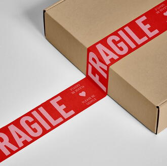 Cardboard box sealed with red tape labeled FRAGILE, used for shipping and handling delicate items