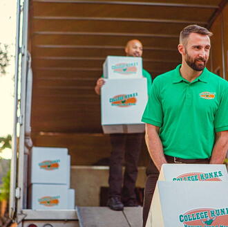 Two College HUNKS movers moving boxes out of the trunk of a moving truck.