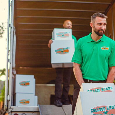 Two College HUNKS movers moving boxes out of the trunk of a moving truck.