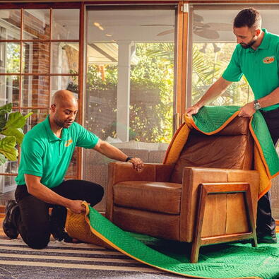 Two College HUNKS movers removing a moving blanket from a chair
