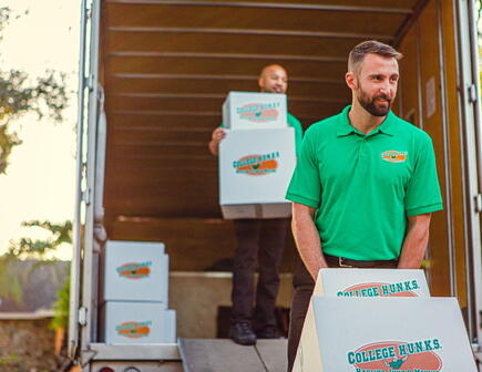 Two College HUNKS movers moving boxes out of the trunk of a moving truck.