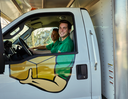 Two College HUNKS movers smiling from the front of a moving truck