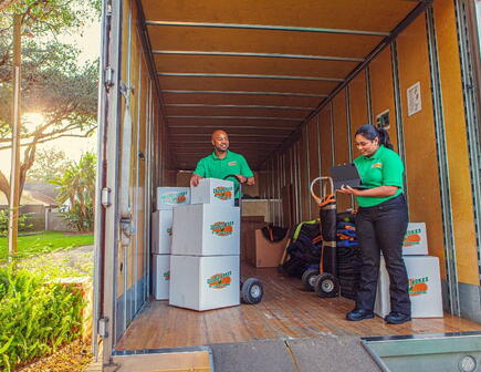 Two College HUNKS movers in the back of a moving truck with boxes.