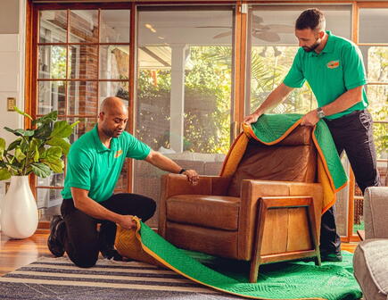 Two College HUNKS movers removing a moving blanket from a chair