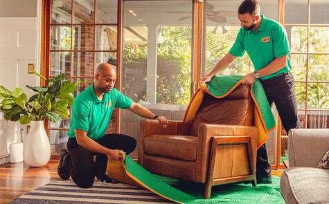 Two College Hunks employees wrapping a couch